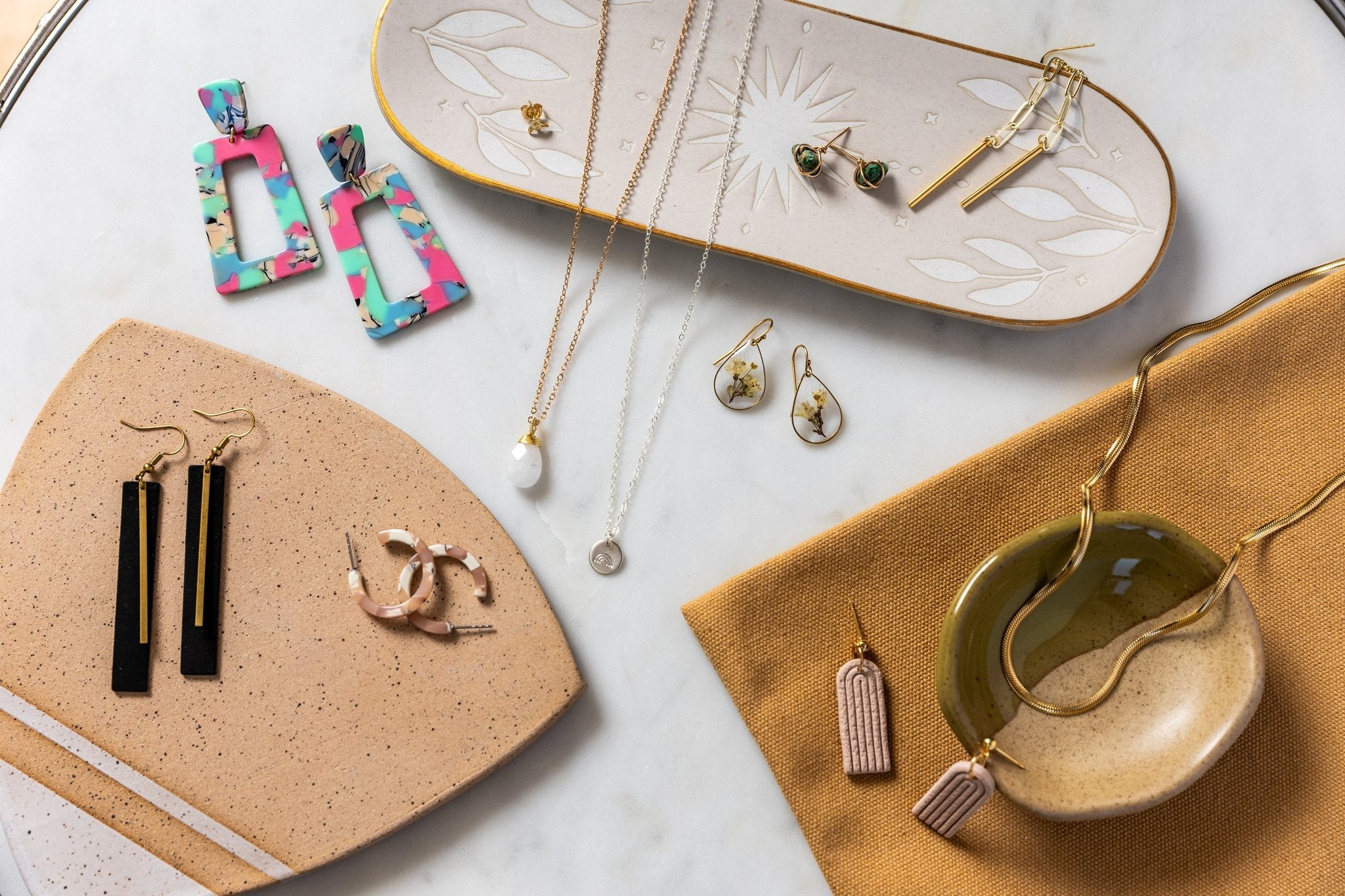 A wide variety of jewelry is arranged artfully on a marble surface and on top of lovely ceramic dishes. All jewelry is available at Khepri Collective.