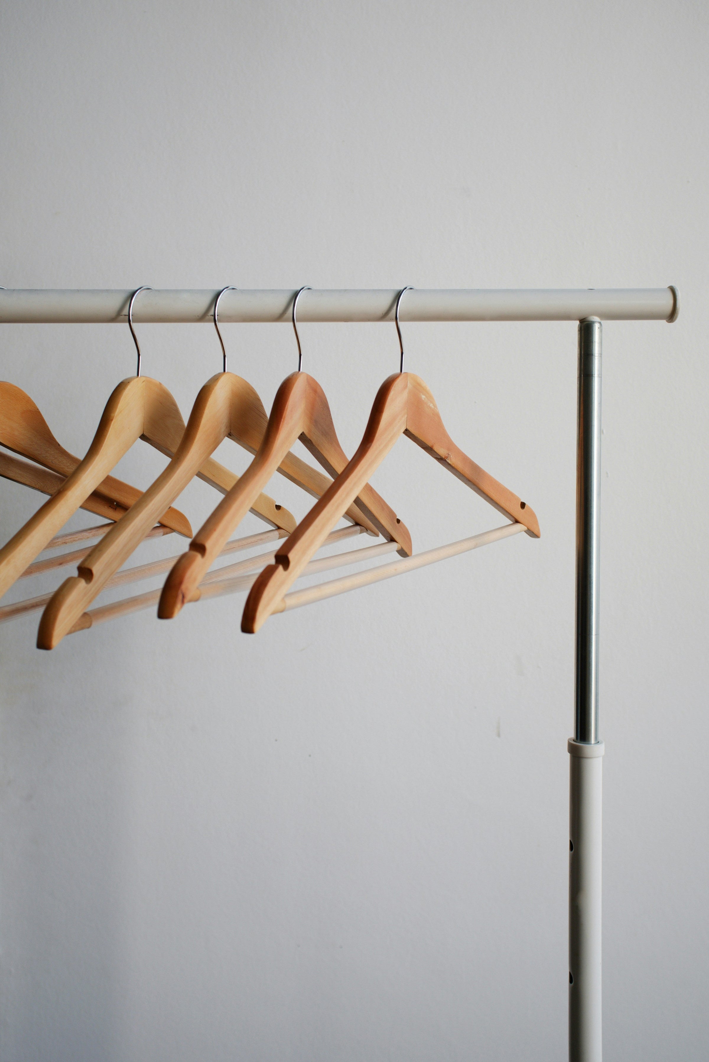 Several empty wooden hangers hang on a metal retail coatrack. 