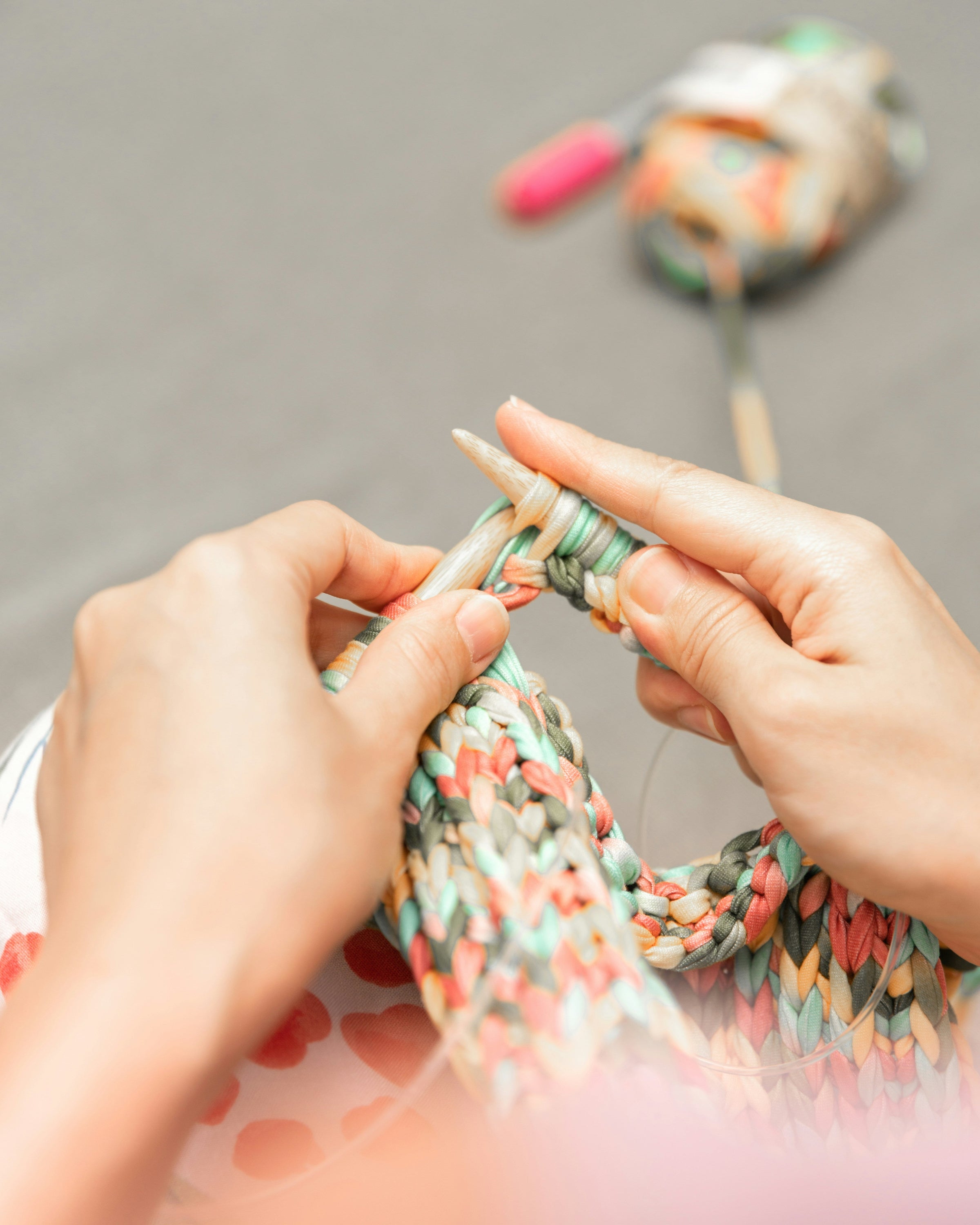 A woman's hands carefully knit a multi-colored scarf. A ball of yarn is below her.